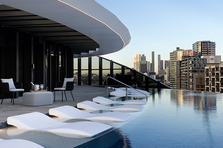 A shot side on of an infinity pool with pool chairs that look out onto the city.